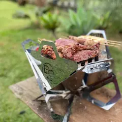 B.C ONYX com carnes assando, vista de perto, com o logo BC cortado na lateral de inox
