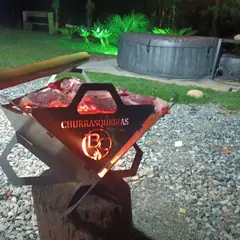 B.C ONYX acesa à noite sobre um tronco, com a brasa iluminando o logo BC Churrasqueiras
