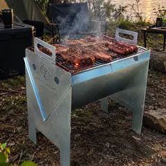 B.C VULKAN com carnes e linguiças na grelha num acampamento à beira do lago, ao pôr do sol